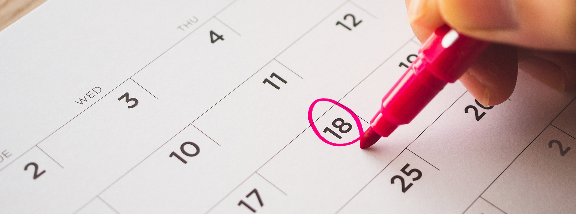 The image shows a close-up of a hand holding a pink highlighter pen, marking the 18th day on a calendar.