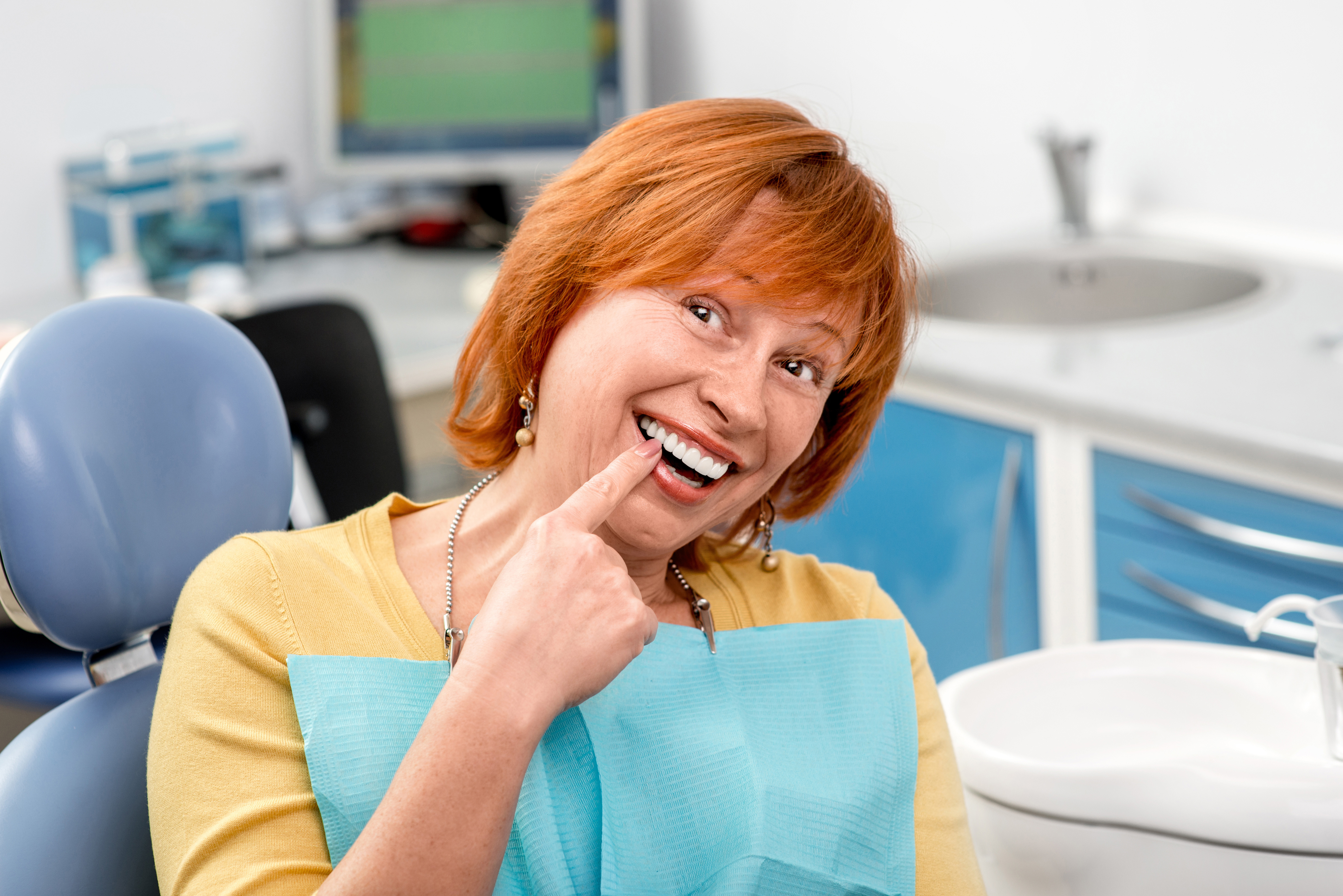 The image shows a woman in a dental office, smiling and pointing at her teeth with a mouthguard on.