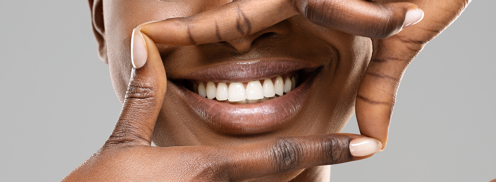 The image shows a smiling person with their hands covering the lower half of their face, which creates an illusion that only the upper part of the face is visible.