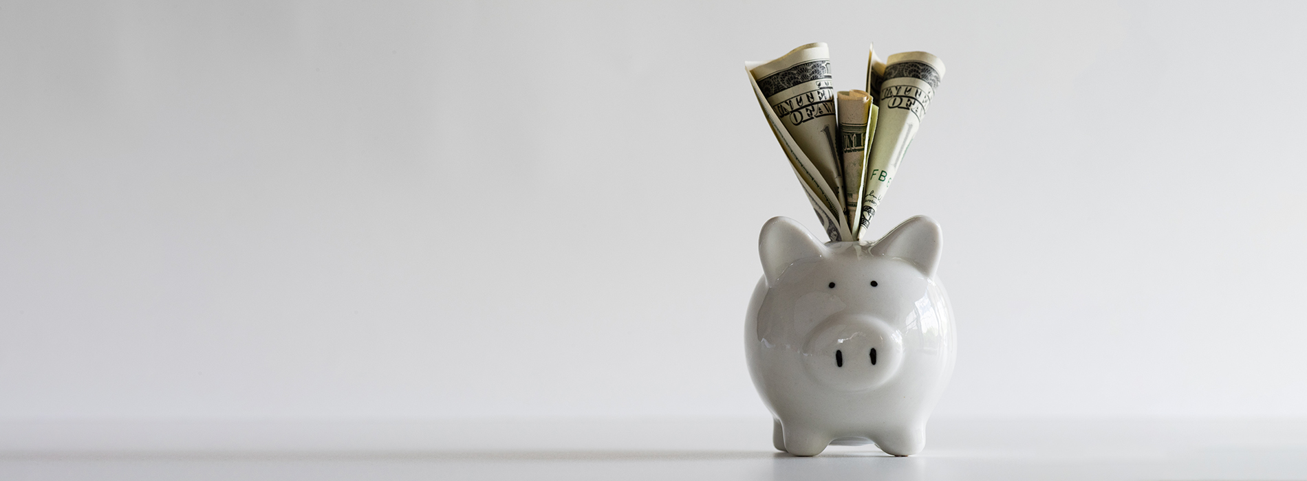 The image shows a piggy bank with money spilling out of it, placed on a surface against a plain background.