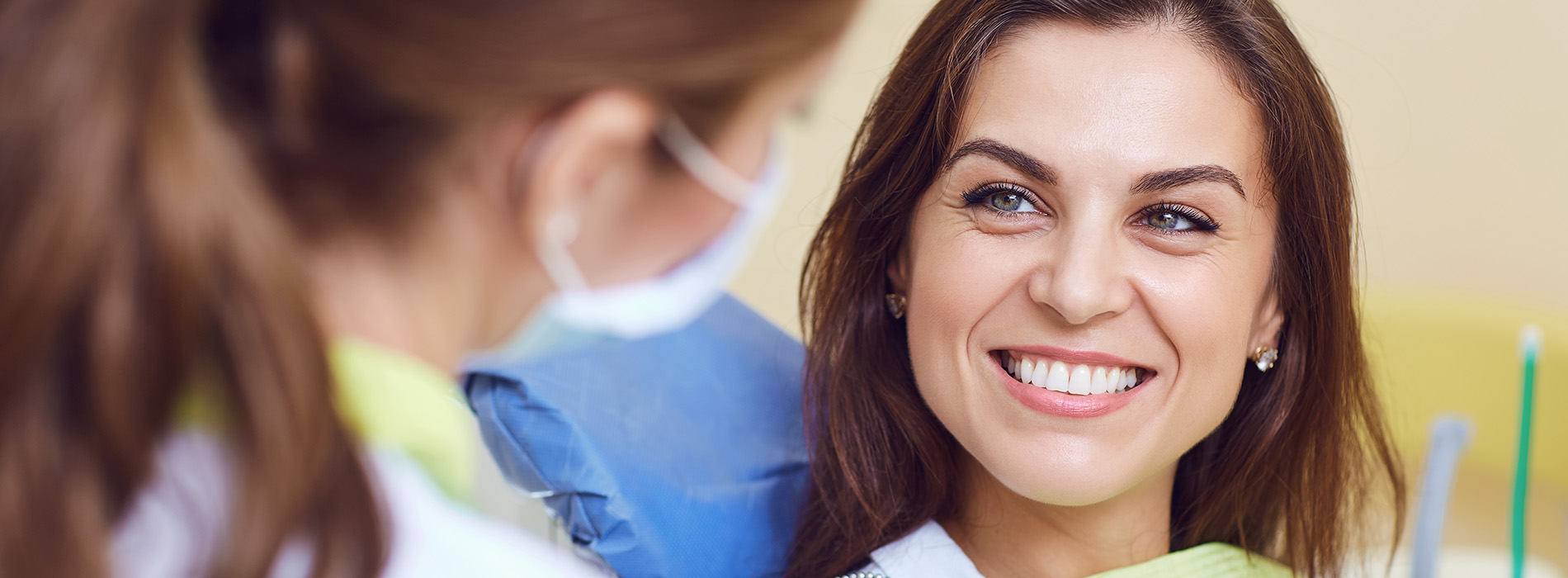 A smiling woman in a dental office, receiving attention from a dentist and dental hygienist.