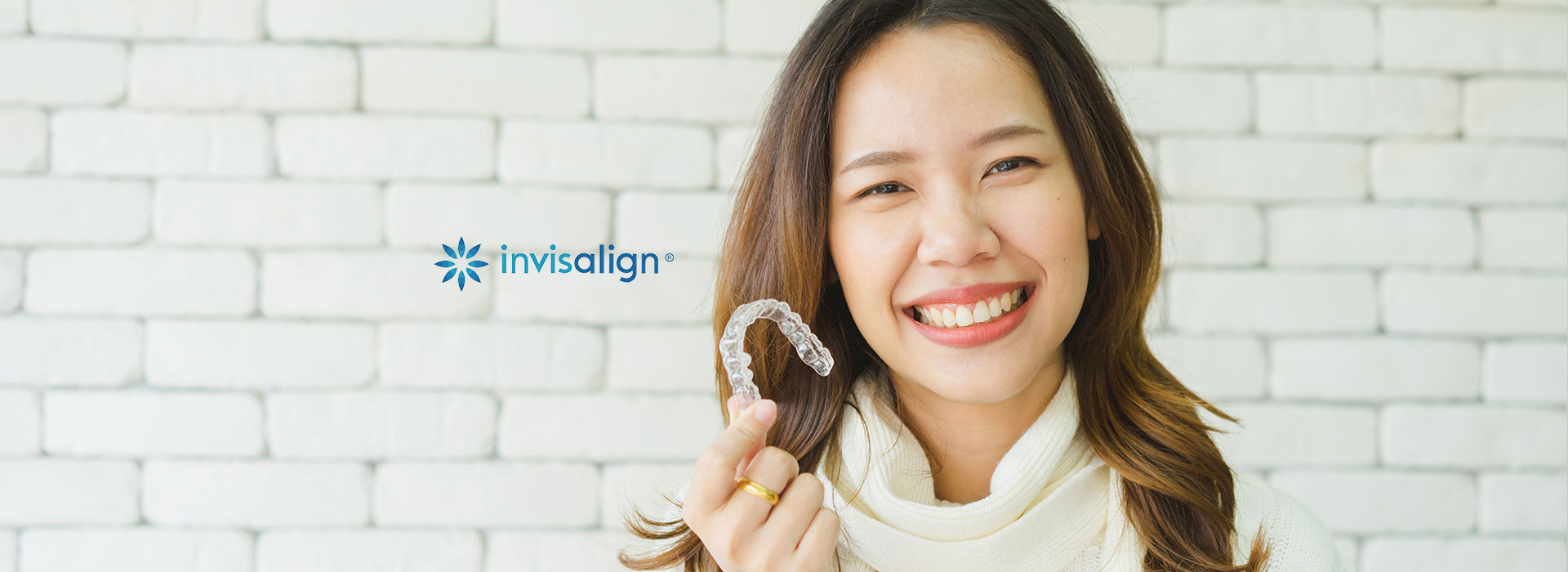 A smiling woman wearing a ring is shown in a close-up, with a watermark that reads  Invision  and a background of a brick wall.