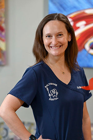 A woman in a blue scrub top stands confidently, smiling at the camera.