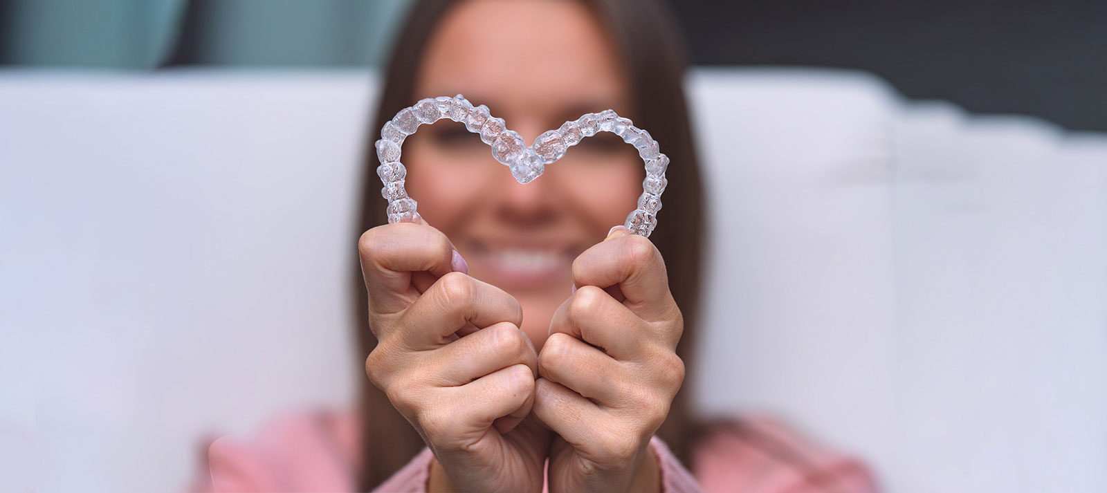 A smiling woman holding a heart-shaped object with the text  Love  on it against a blurred background.