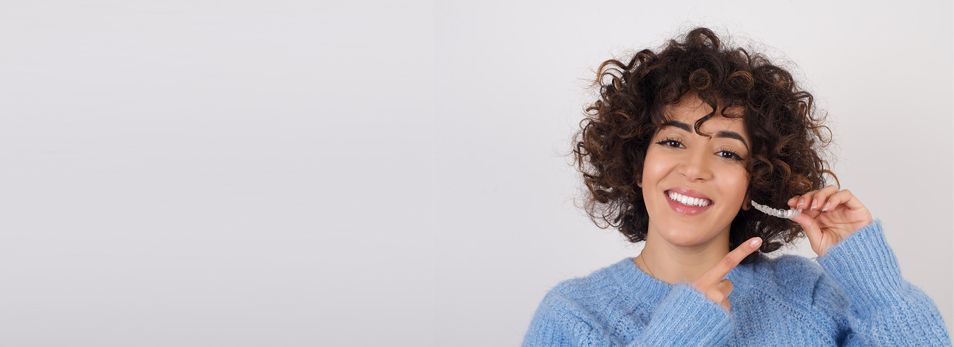 The image features a person with curly hair, smiling and holding a smartphone to their ear, against a plain background.