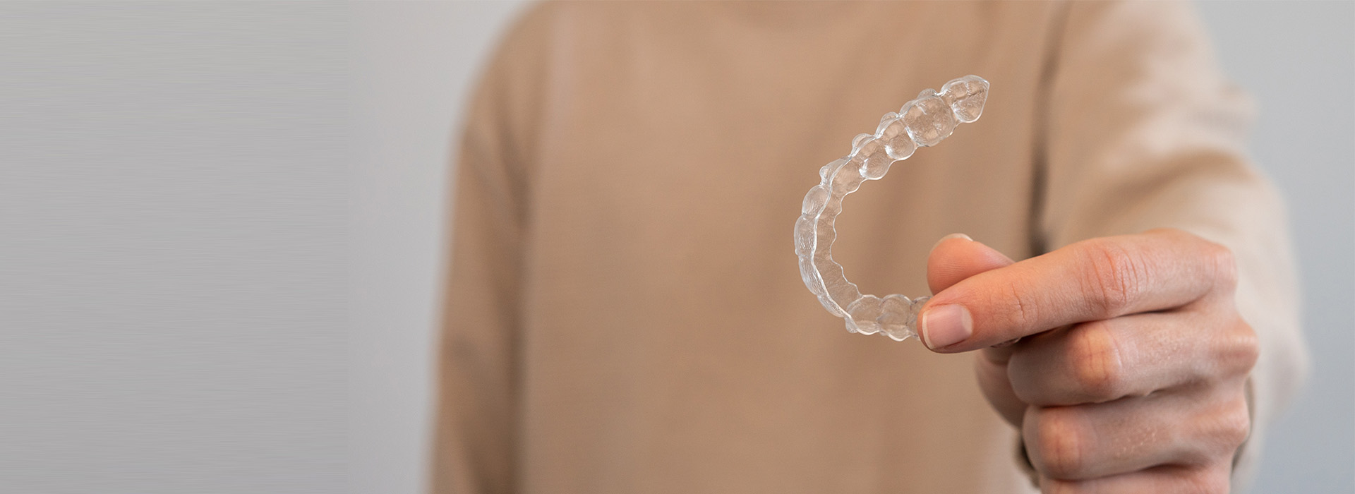 A hand holding a transparent soap bubble against a plain background.