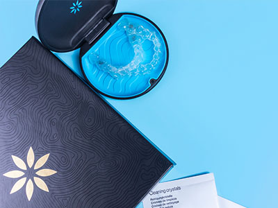 A blue toothbrush case with a toothbrush inside, placed next to an open box of dental crystals on a light blue background.