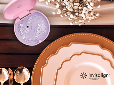 The image is a promotional advertisement for Invisalign, featuring a table setting with place settings and a box of Invisalign aligners.