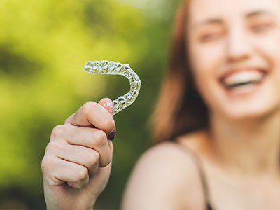 A smiling woman holding a clear plastic dental retainer.