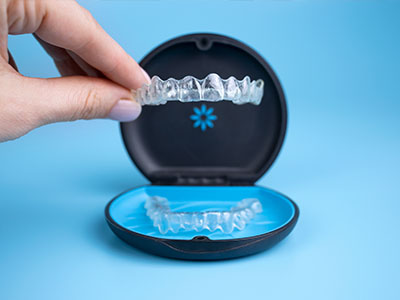 The image shows a hand holding an open clear case containing a set of transparent dental aligners, with the brand name  Invisalign  visible on the case.