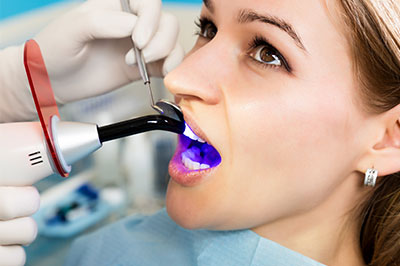 A woman receiving dental treatment, with a dental hygienist using an ultrasonic scaler to clean her teeth.