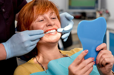 A woman receiving dental care, with a dental professional holding up a blue model of a mouth and teeth.