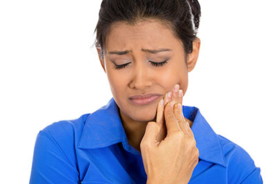 A woman with a worried expression is holding her face, possibly indicating pain or discomfort.