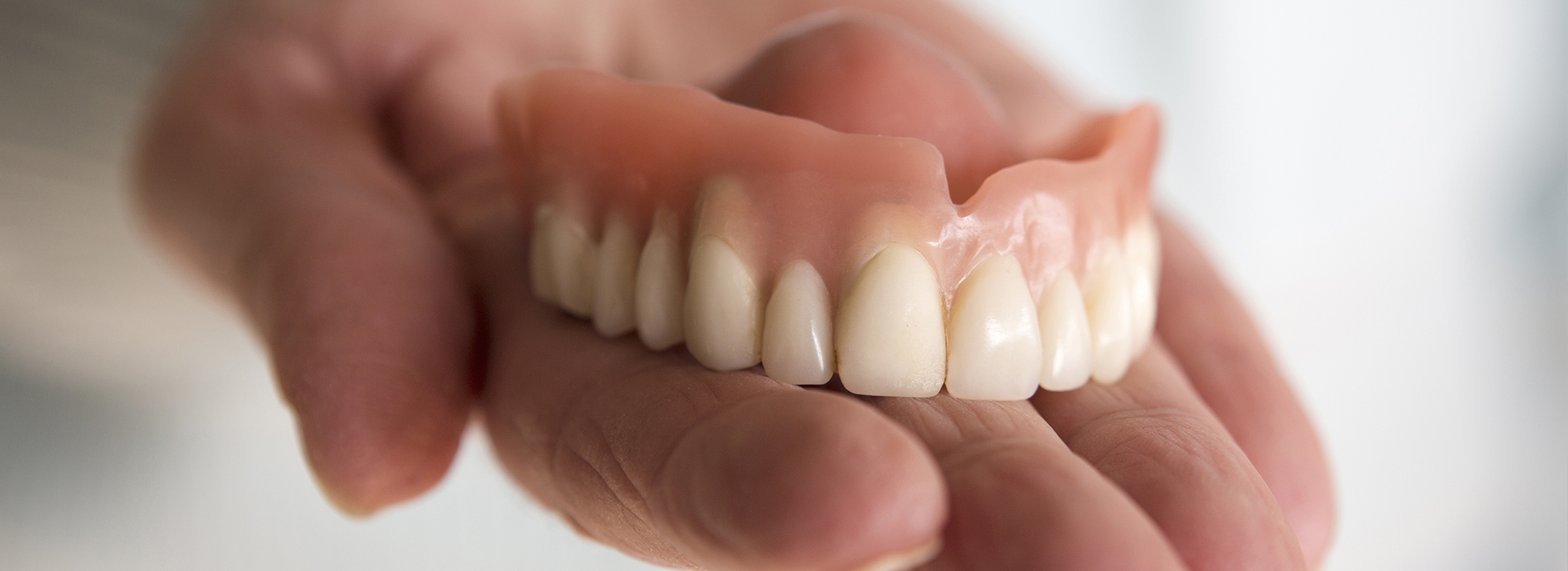 Hand holding a set of dentures, showcasing the upper and lower dental arches.