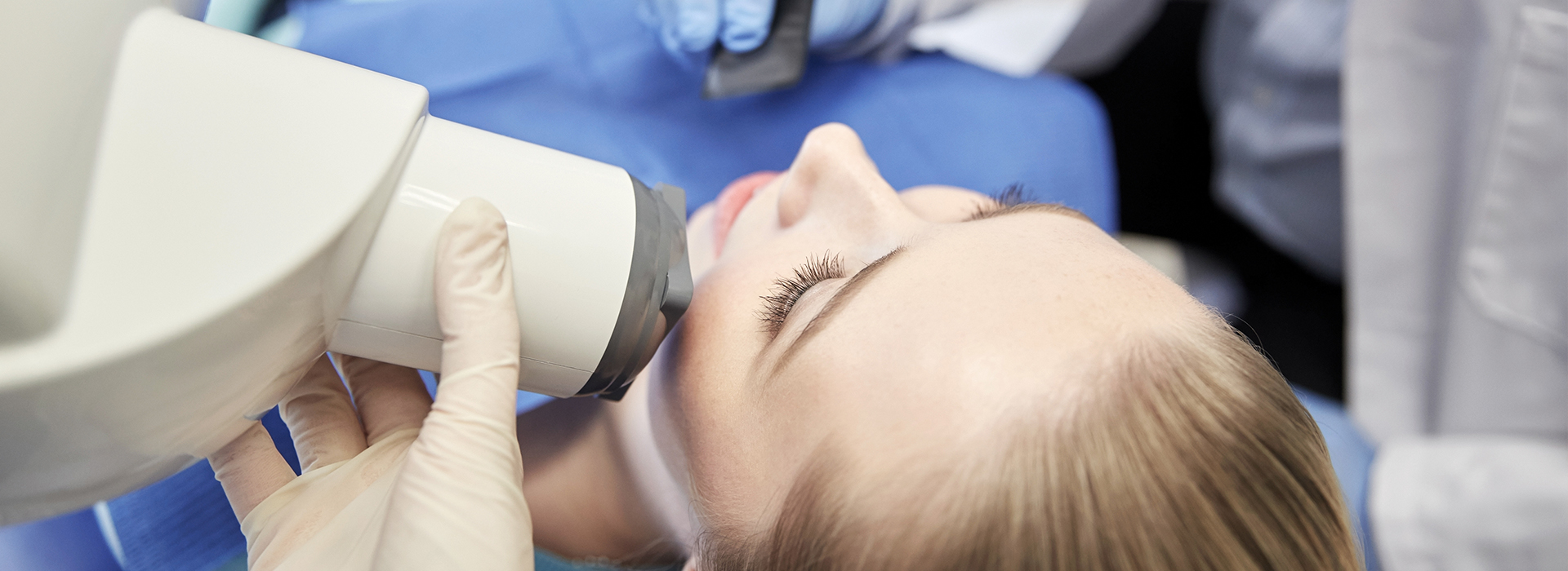 The image shows a person receiving dental care, with a focus on the dental professional using a microscope to examine the patient s teeth.