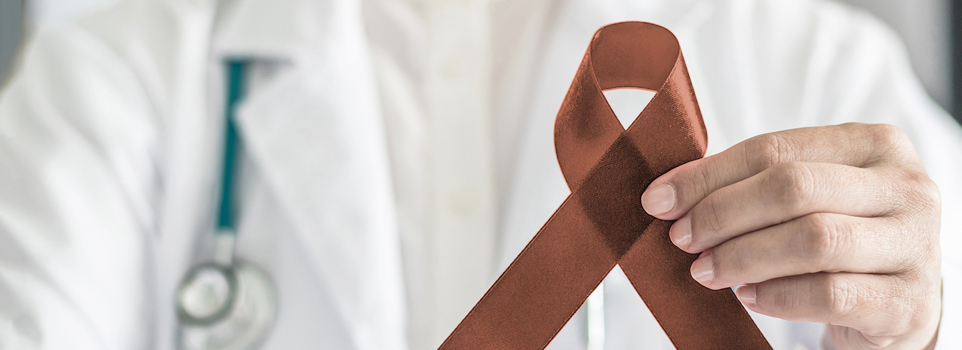 A healthcare professional holding a brown ribbon with a red heart symbol, commonly associated with awareness for heart disease.