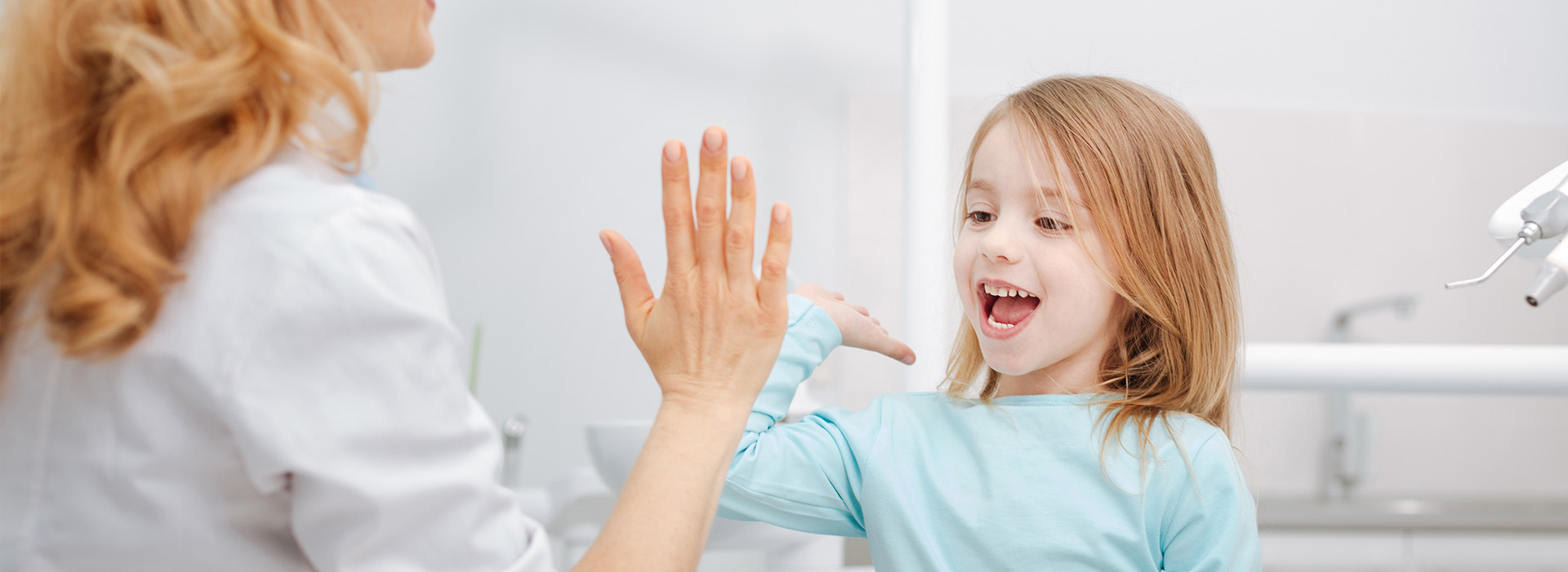 A woman and a young girl in a dental office, with the woman holding up her hand towards the child.