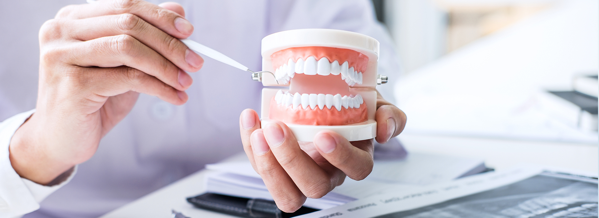 A person s hand holding a toothbrush in front of an open mouth, with a computer monitor displaying a dental software interface.