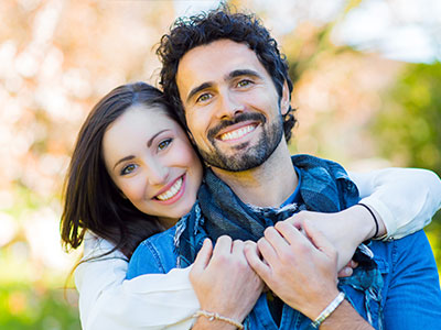 A man and a woman embrace each other in a joyful pose, both smiling broadly.