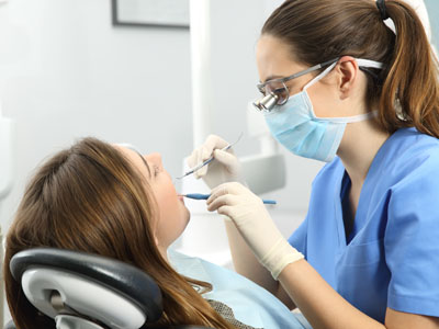 An image featuring a dental hygienist assisting a patient during a dental appointment, with the hygienist wearing protective gear and using instruments.