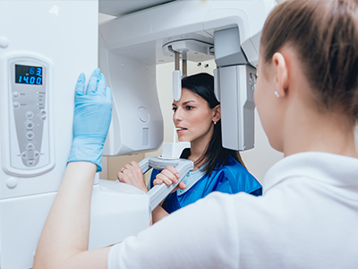 An image featuring a woman in a blue lab coat standing next to a large, modern 3D scanner, with a man wearing white gloves and a black face mask inspecting the equipment.