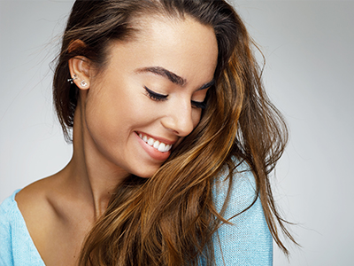 A woman with long hair, smiling and looking to the side, against a plain background.