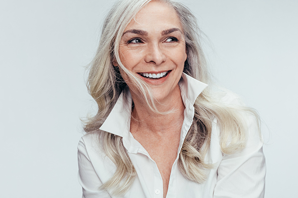 The image features a woman with short hair, wearing a white top, smiling and looking directly at the camera.